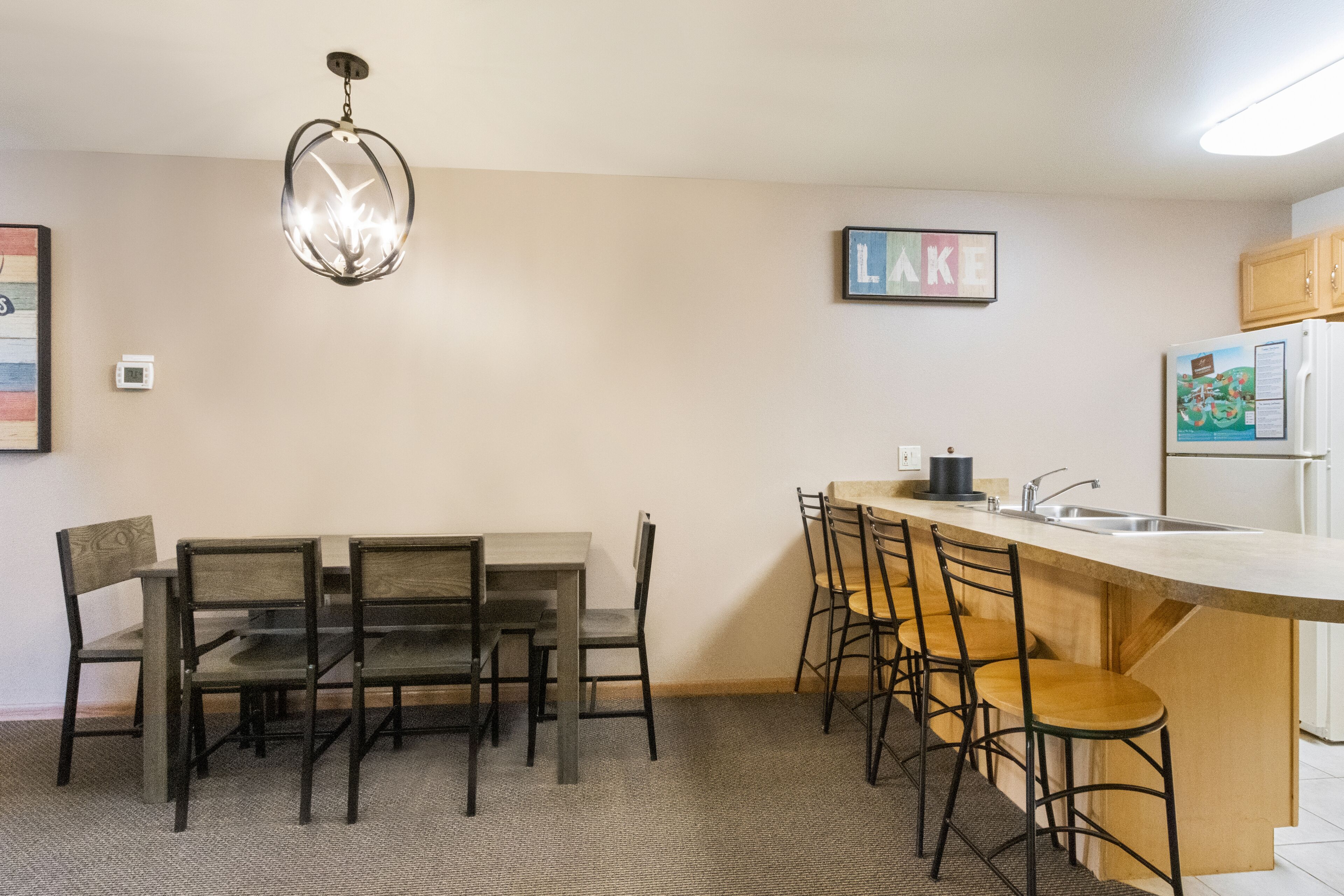 A compact kitchen with a dining table and bar stools, a refrigerator, and a pendant light.