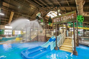 An indoor water park with a 'Welcome' sign, slides, and a hot tub area.