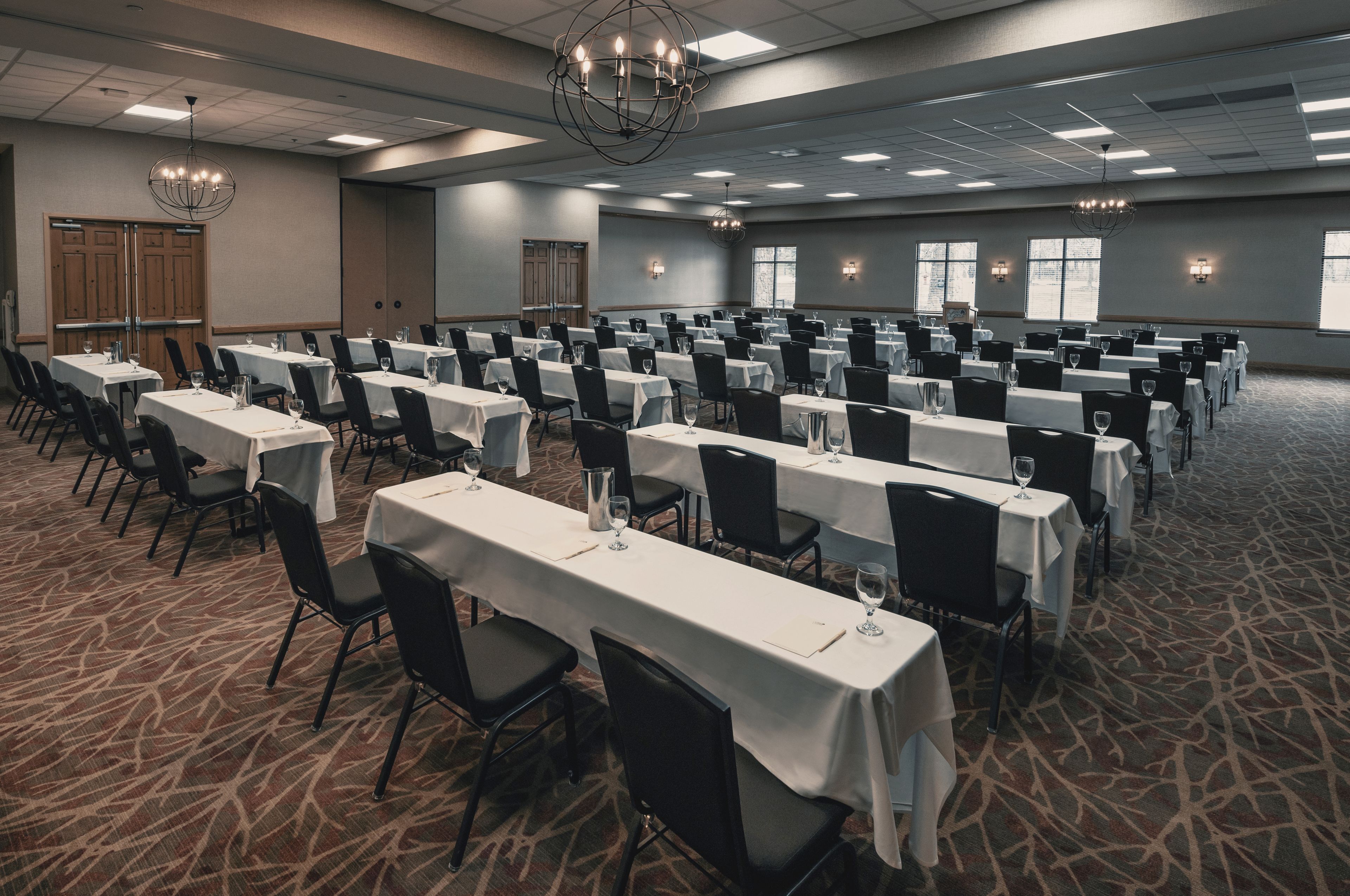 A conference room with rows of tables and chairs, large windows, and chandeliers.