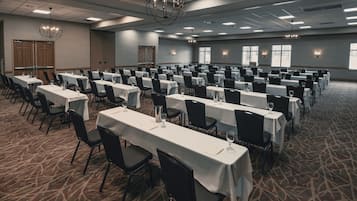 A conference room with rows of tables and chairs, large windows, and chandeliers.