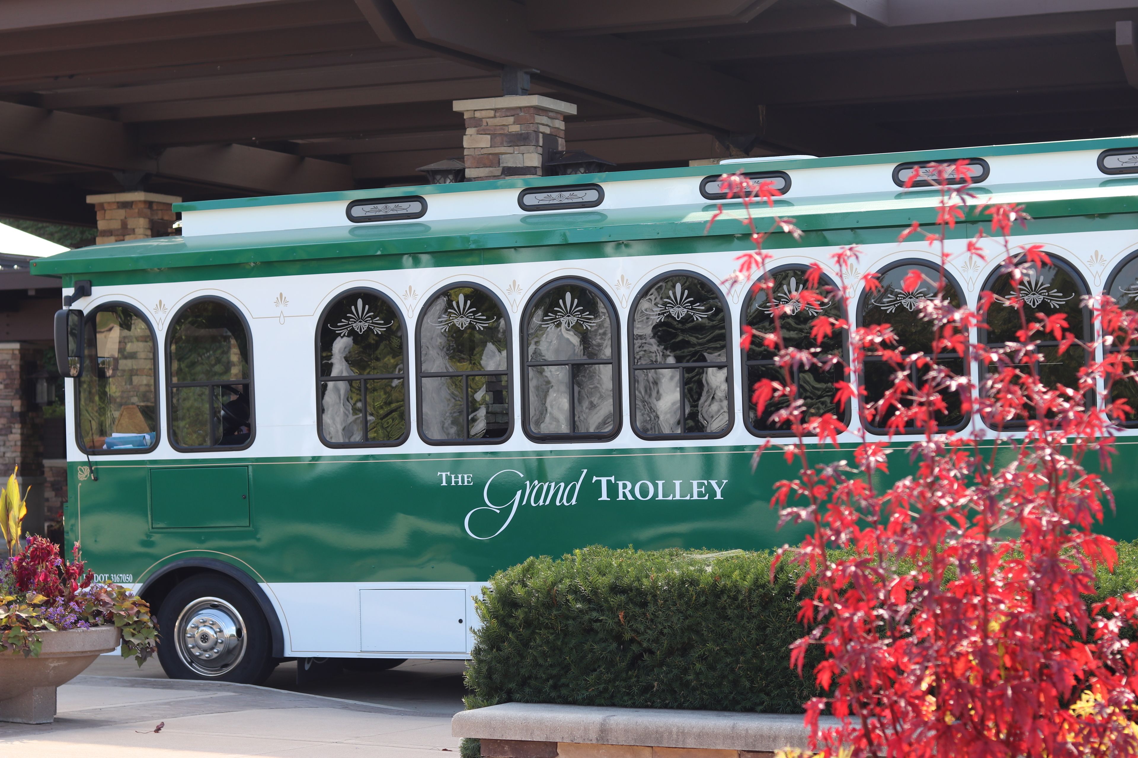 A green and white trolley with decorative windows and the text "The Grand Trolley" on its side.