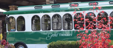 A green and white trolley with decorative windows and the text "The Grand Trolley" on its side.