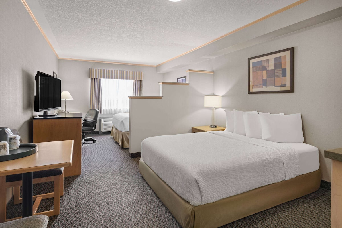 A hotel room with a large bed, a desk with a chair, a television, and a small table.