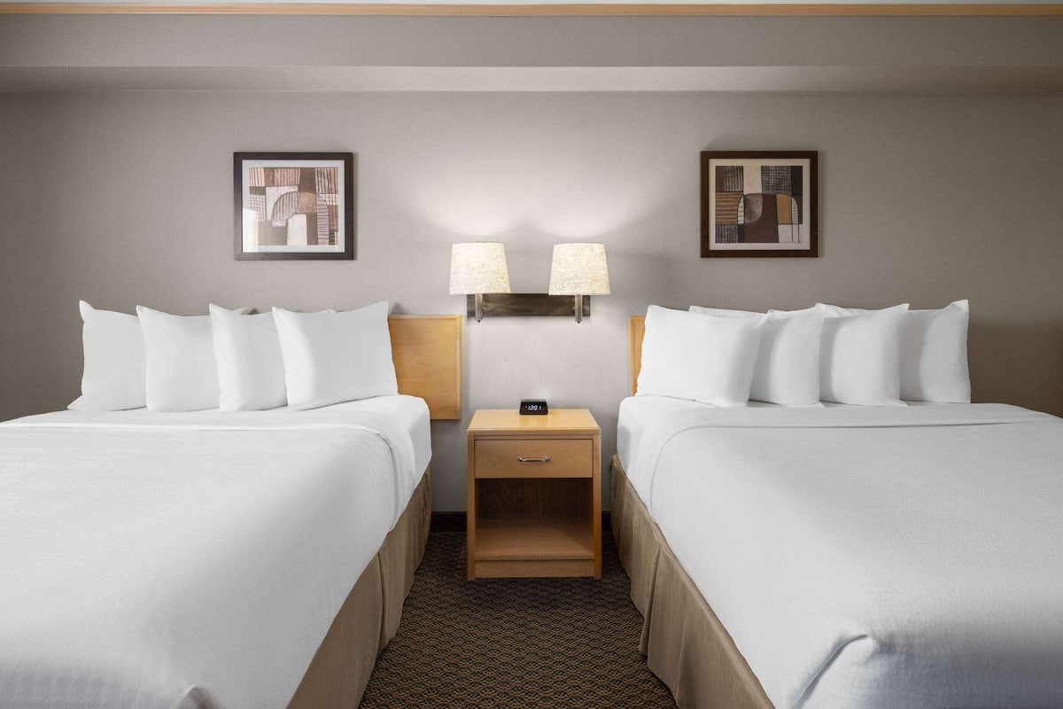 A hotel room with two beds, a nightstand with a lamp, and framed artwork on the walls.