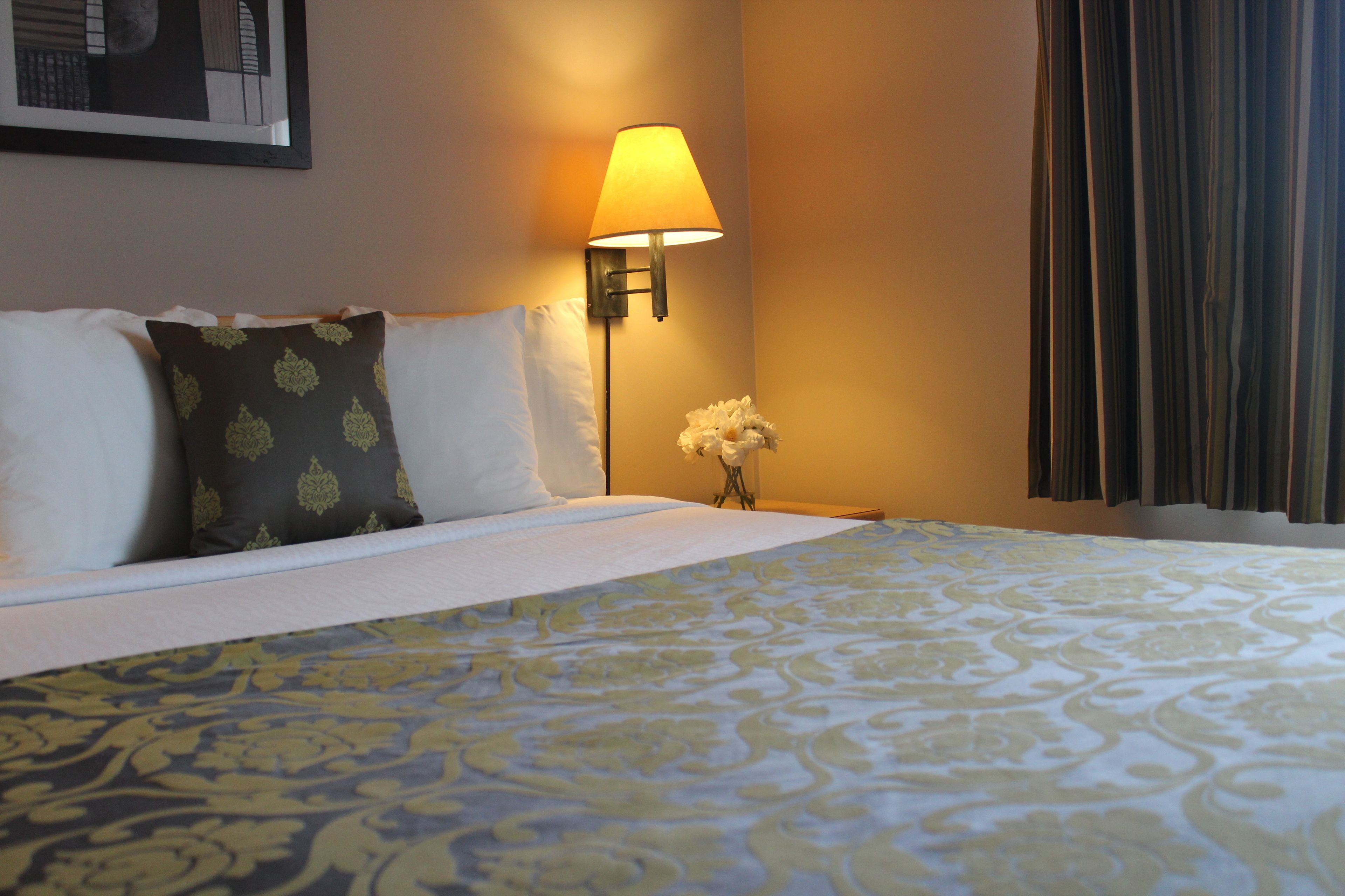 A hotel room with a neatly made bed, a bedside lamp, a vase with flowers, and a framed picture on the wall.