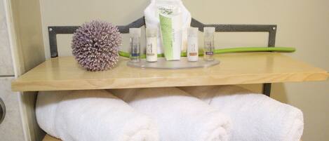A bathroom shelf with toiletries, a bath sponge, and rolled towels.