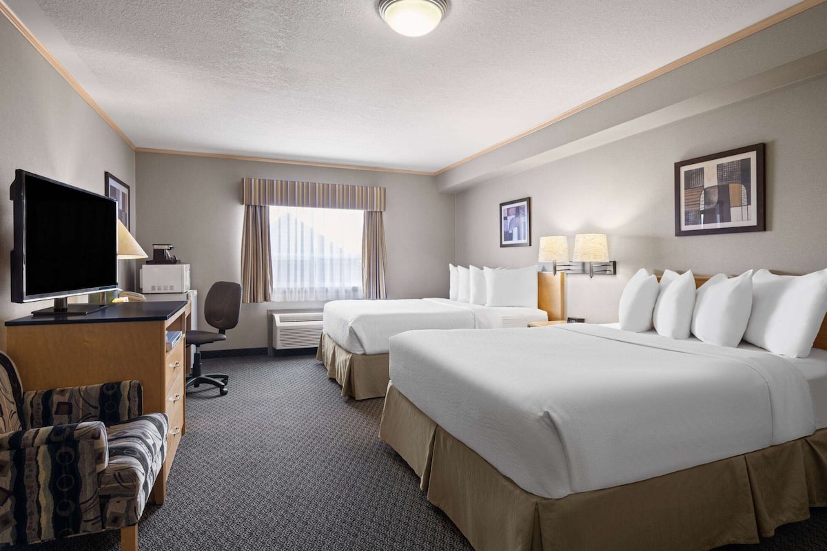 A hotel room with two beds, a desk with a computer, a TV, and a chair.