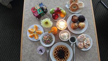 Une table de petit-déjeuner avec divers aliments, notamment des gaufres, des pâtisseries, des fruits et des boissons.