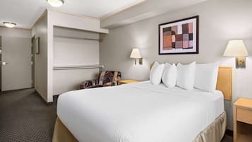 A hotel room with a large bed, a chair, a desk, and a wall-mounted lamp.