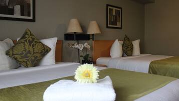 Habitación de hotel con dos camas, cada una con cubrecama verde y ropa de cama blanca. Hay almohadas decorativas, una mesita de noche con lámpara y un cuadro en la pared.