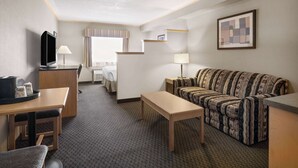 A hotel room with a sofa, a small table, a TV, a desk, and a bed.