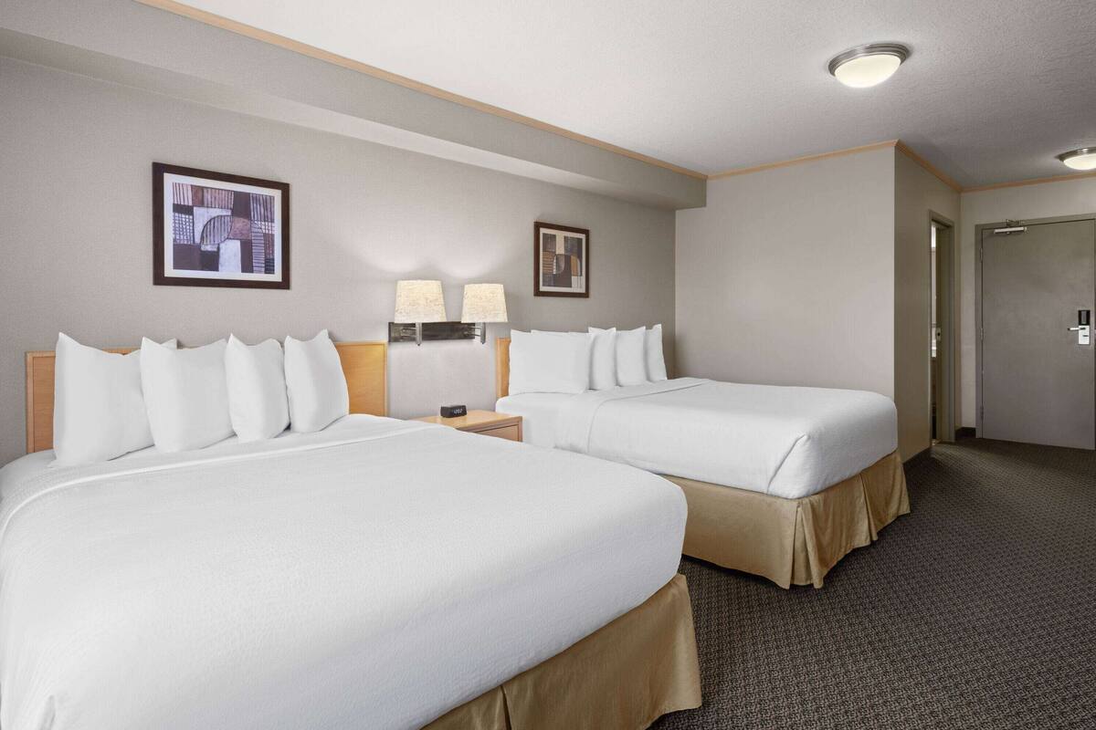A hotel room with two beds, a nightstand with lamps, and a door.