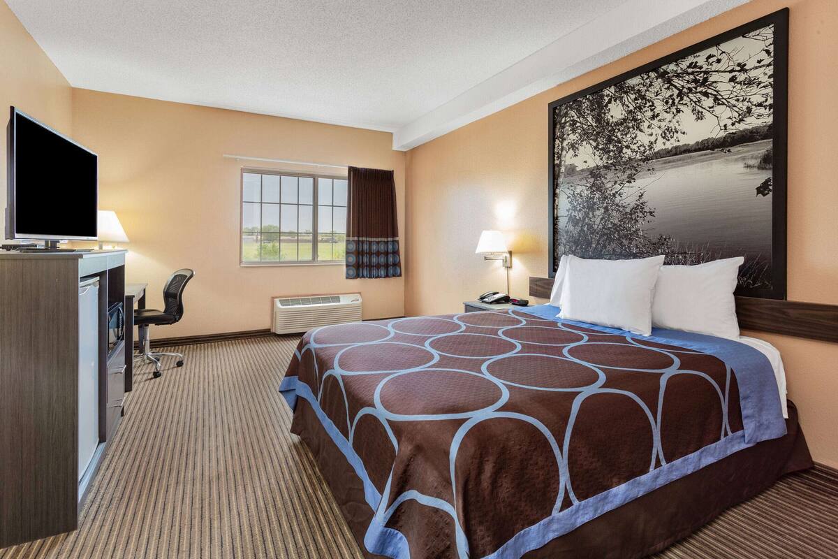 Une chambre d’hôtel avec un lit, un bureau avec un ordinateur, une télévision et une fenêtre avec des rideaux.