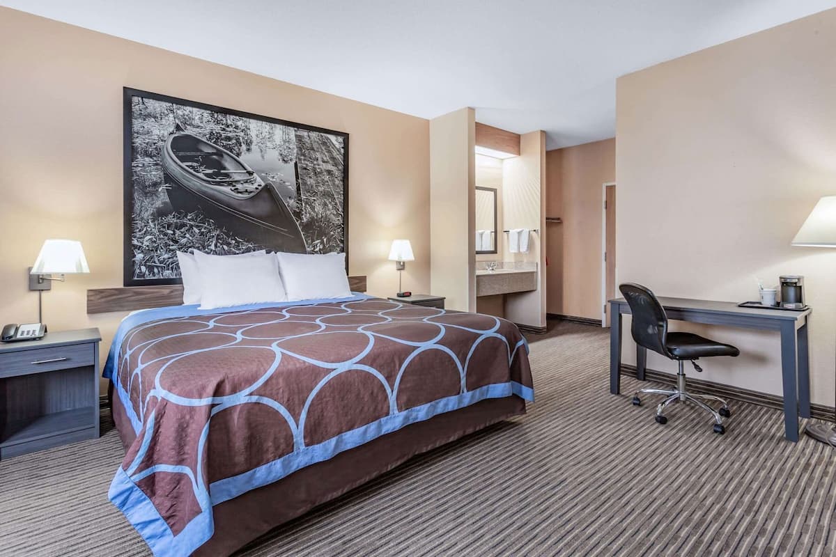 Une chambre d’hôtel comprenant un lit, un bureau, une chaise, une table de chevet, une lampe, un téléphone et un grand tableau encadré au mur.
