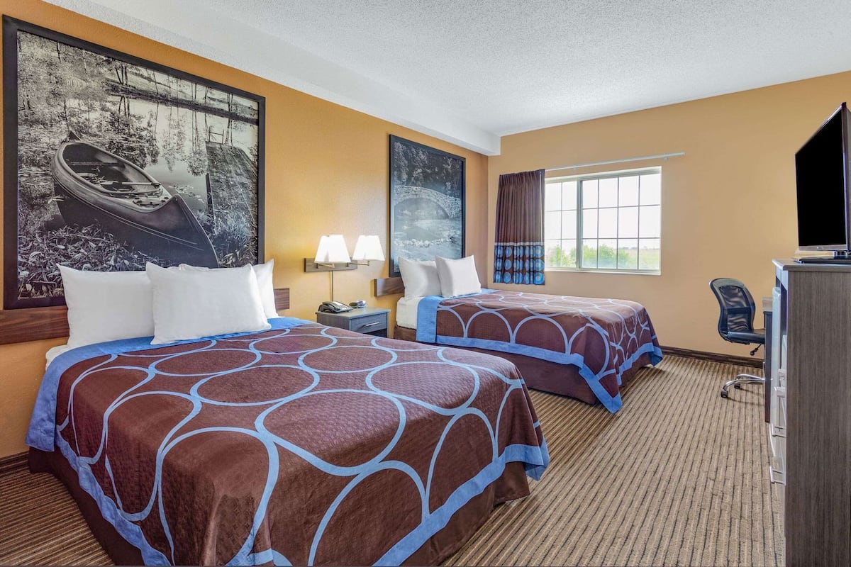 Une chambre d’hôtel avec deux lits, un bureau, une télévision et de grandes fenêtres.