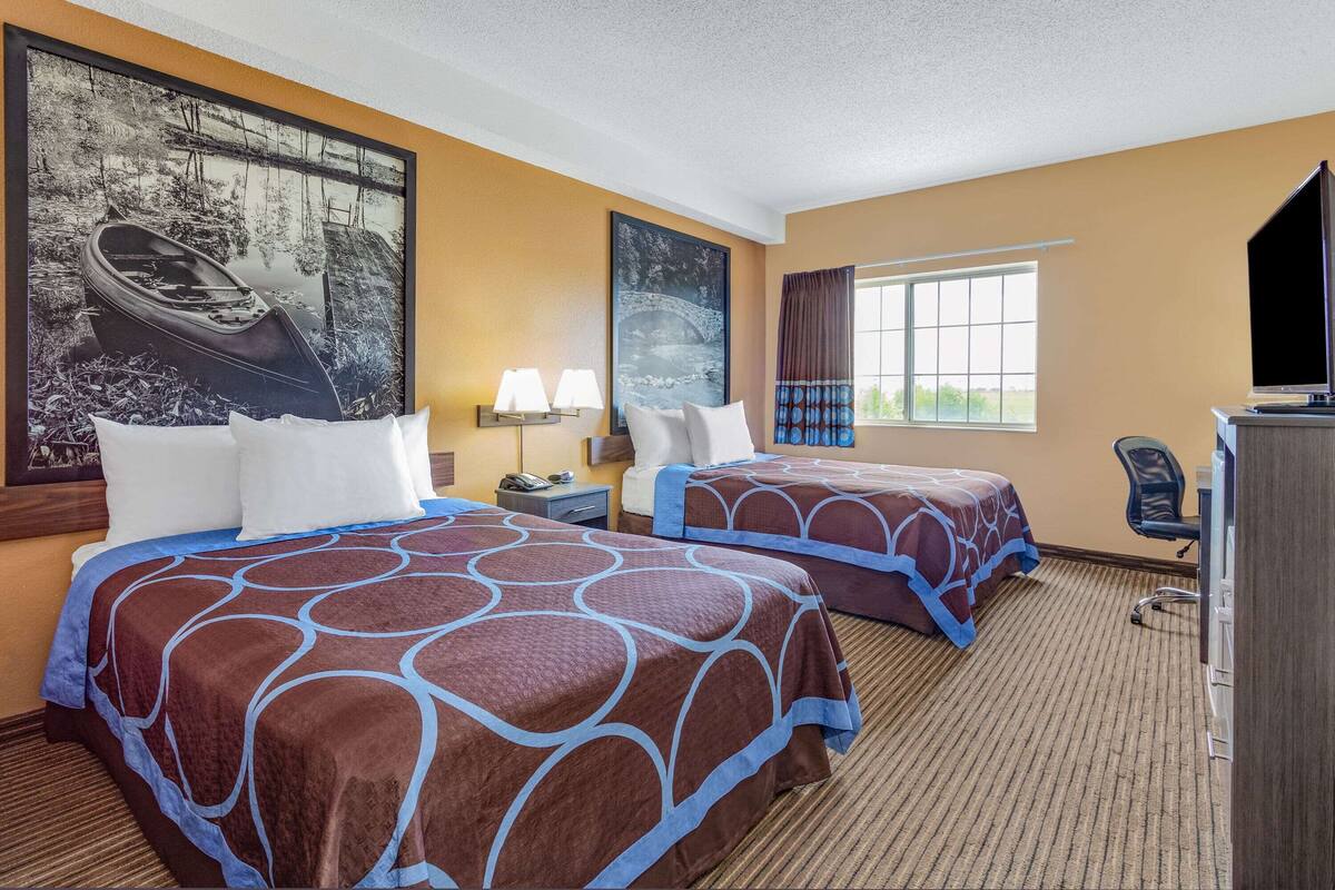 Une chambre d’hôtel avec deux lits, une grande fenêtre, un bureau, une chaise et un téléviseur.