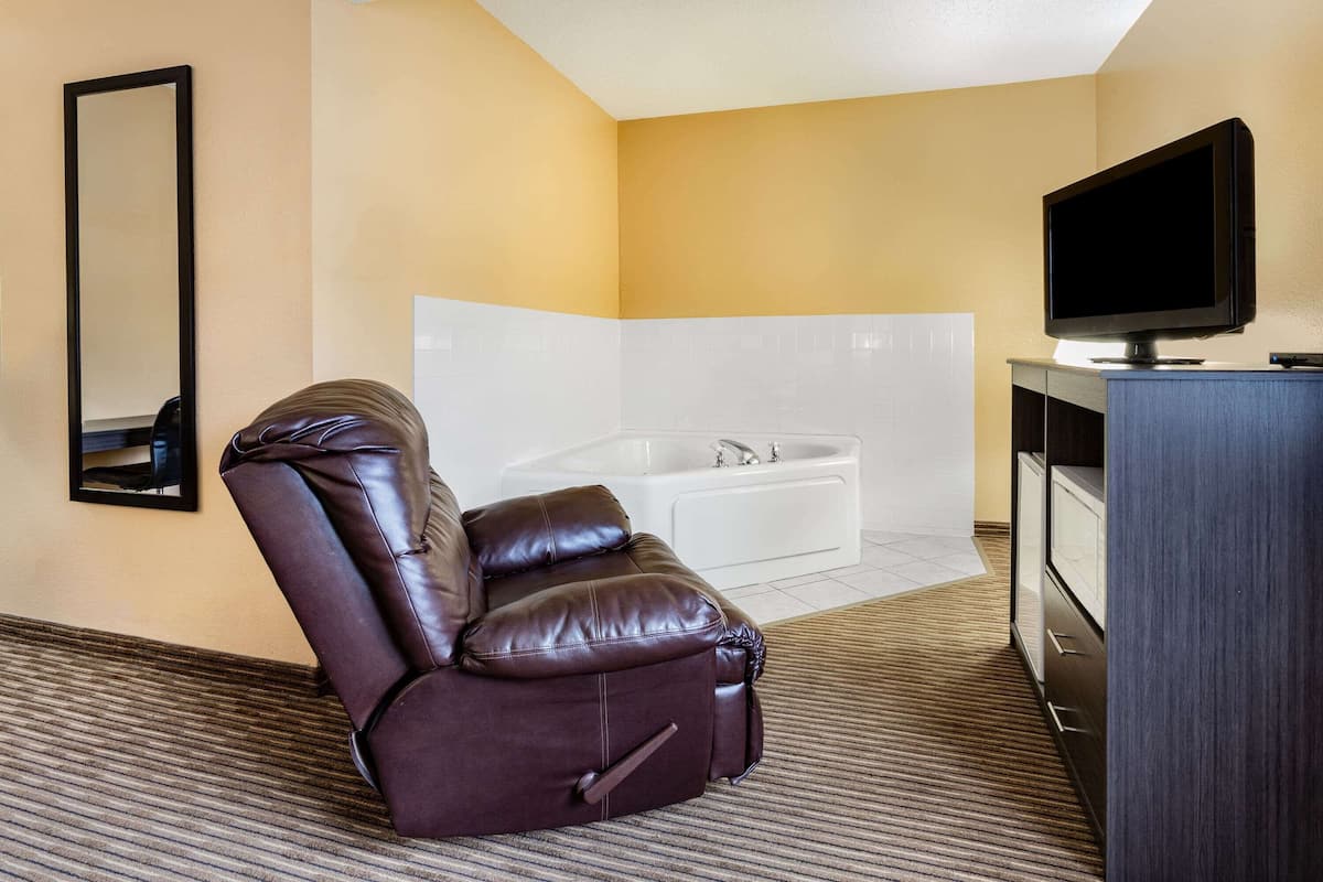 Une chambre d’hôtel avec un fauteuil inclinable en cuir, un téléviseur à écran plat, une baignoire blanche et un grand miroir.