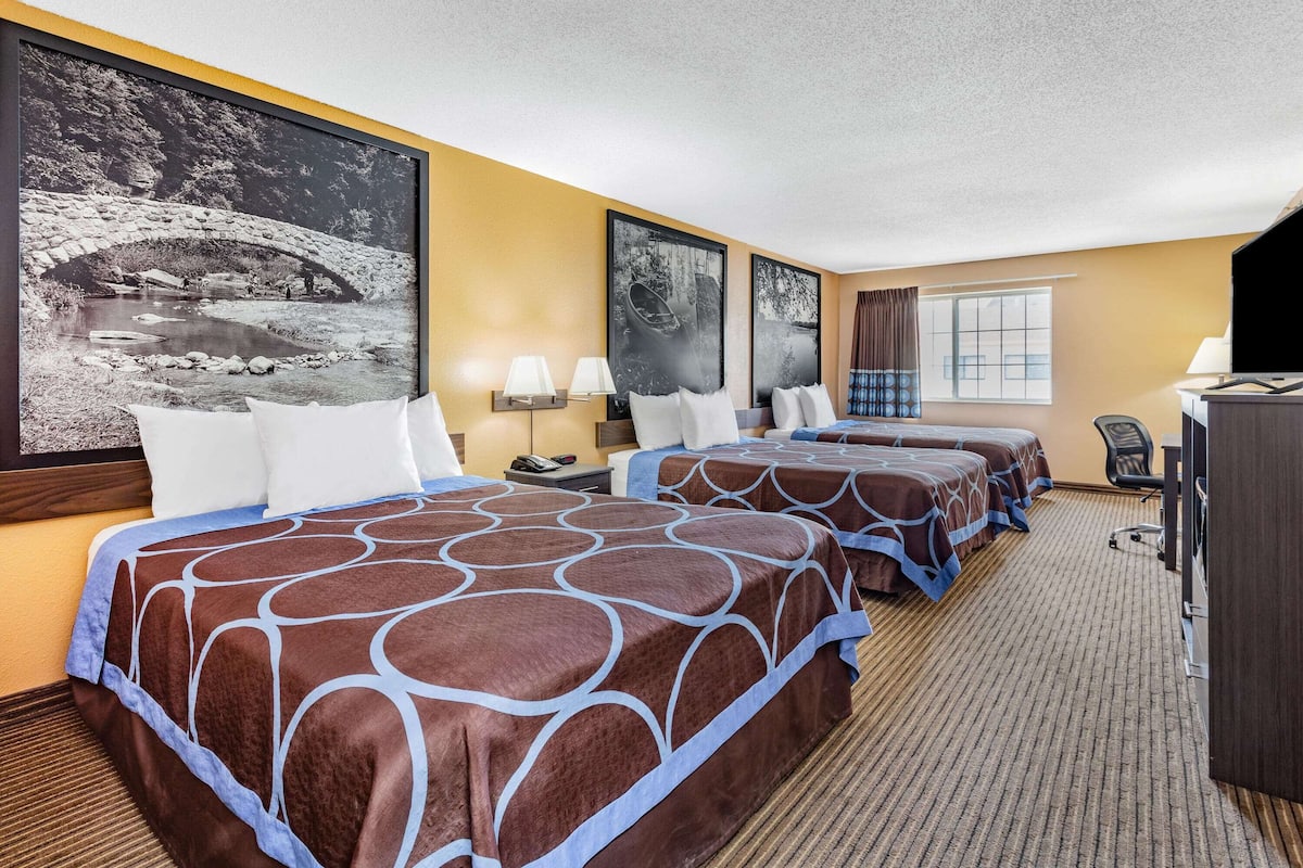 Une chambre d’hôtel avec trois lits, une télévision, un bureau et une grande fenêtre.