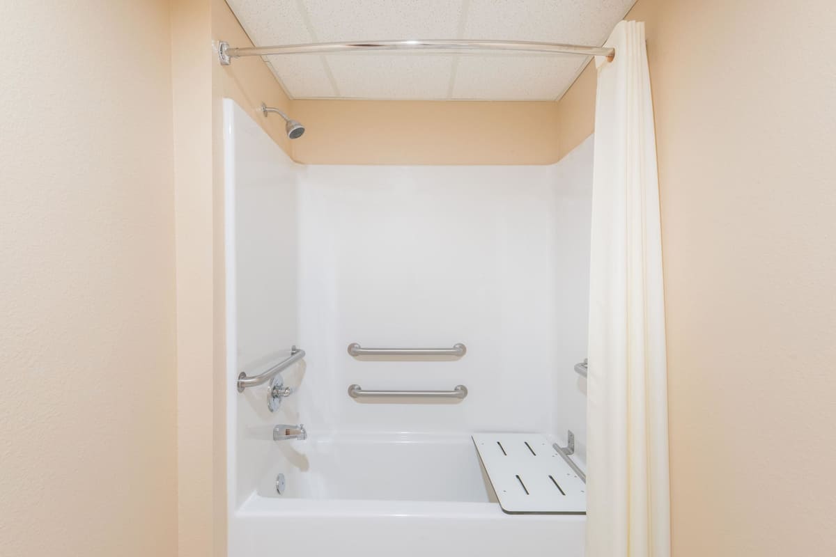 Une baignoire blanche standard, équipée de barres d’appui, d’un pommeau de douche et d’un panneau de commande.