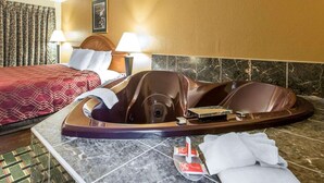 Une chambre d’hôtel avec une grande baignoire, un lit recouvert d’une couverture rouge, deux lampes de chevet et un tableau accroché au mur.