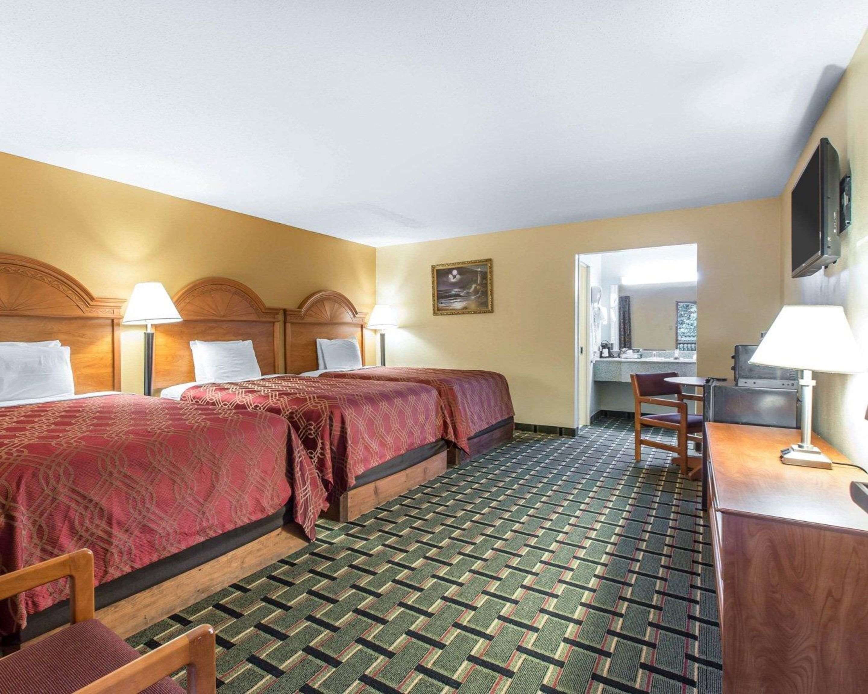 Ein Hotelzimmer mit zwei Betten, einem Schreibtisch, einem Stuhl und einem durchgegangenen Badezimmer.