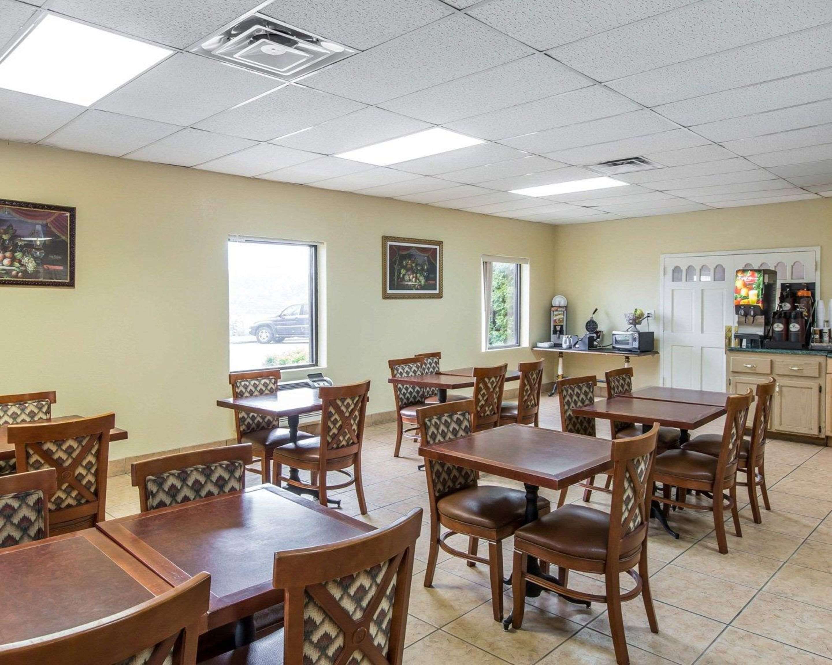 A dining area with multiple wooden tables and chairs, a kitchen area with appliances, and framed artwork on the walls.
