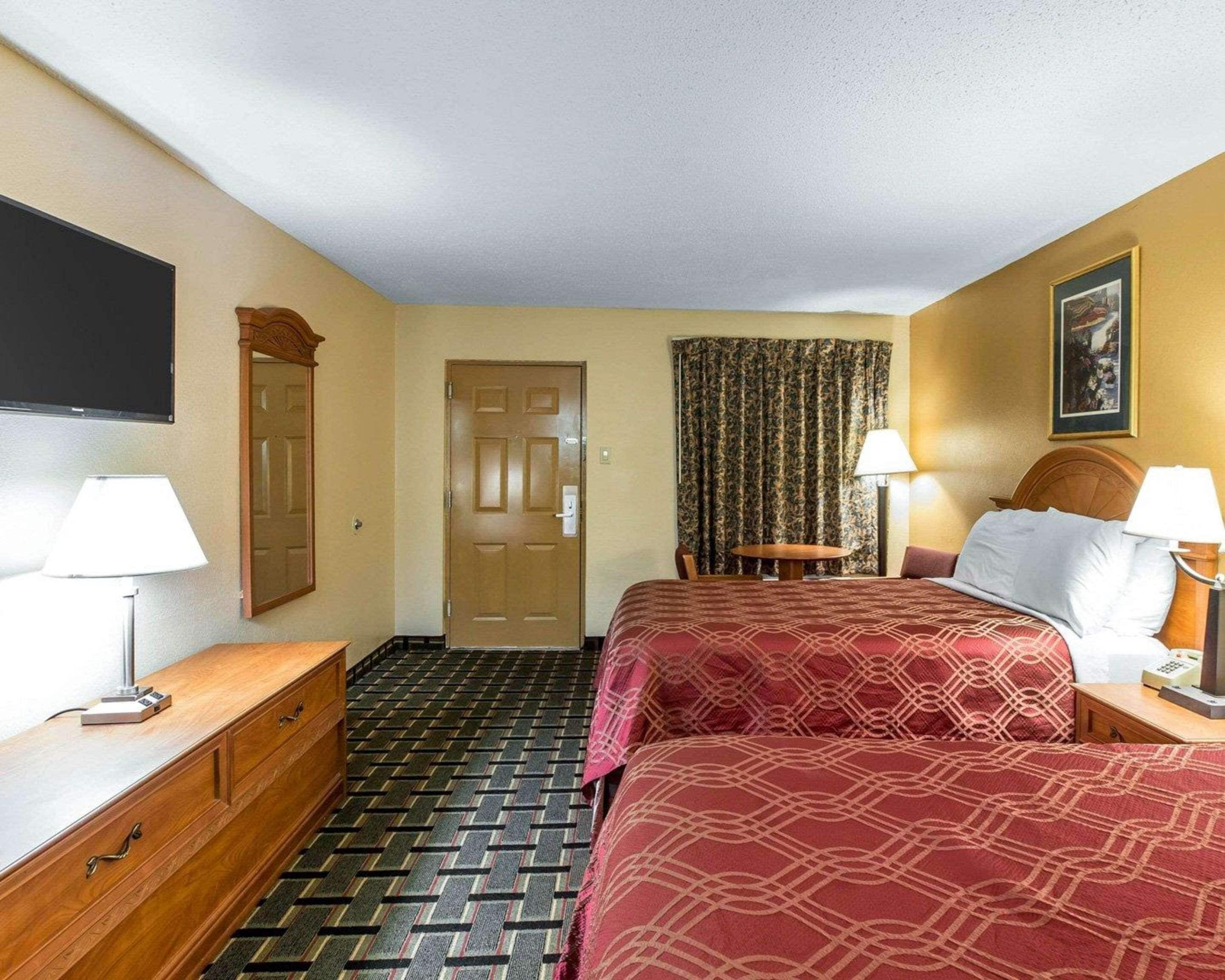 Habitación de hotel con cama, escritorio, silla, televisor y puerta.