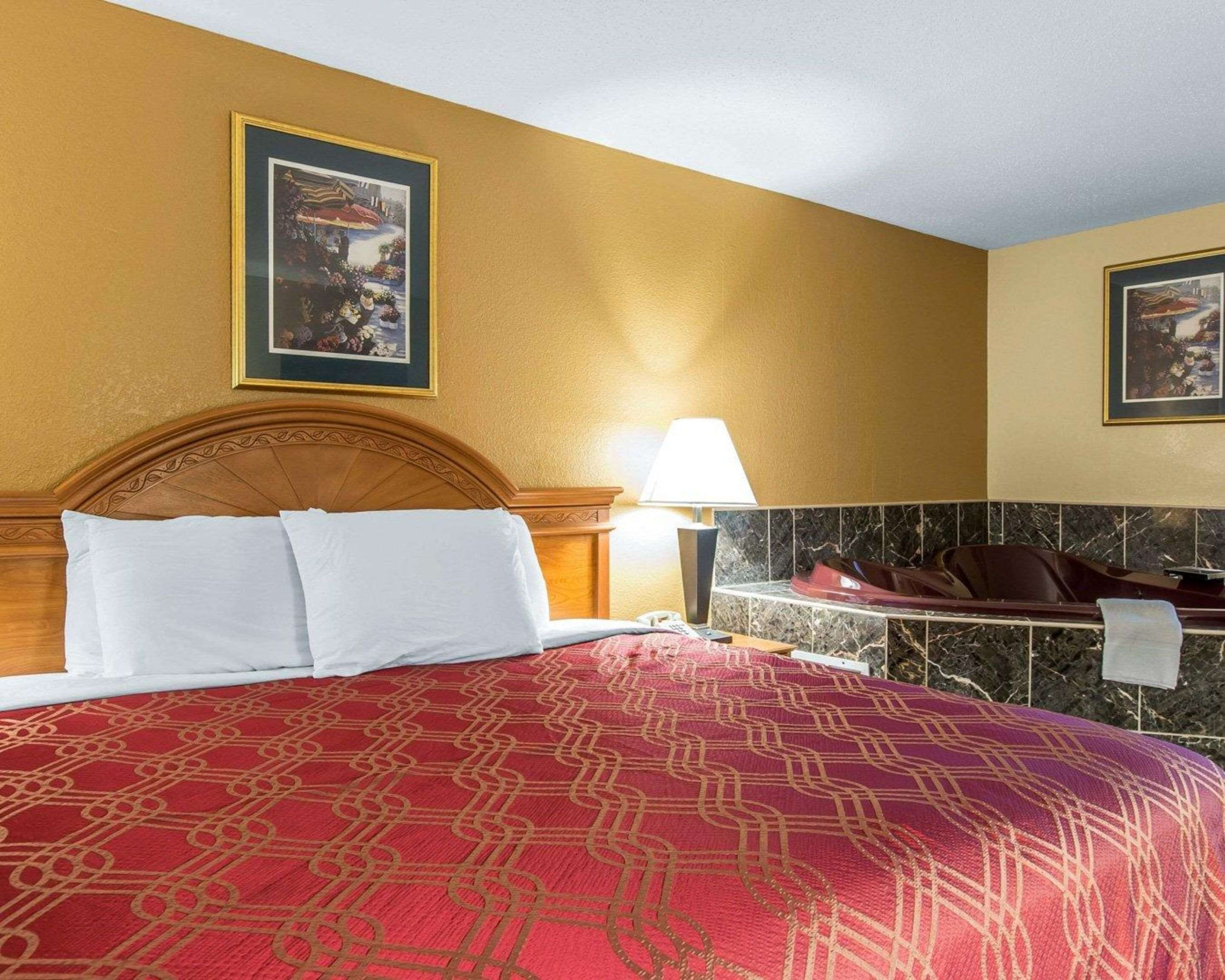 A hotel room with a large bed, a headboard, a nightstand with a lamp, a marble-tiled wall, and two framed pictures on the wall.