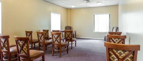 Un salón de conferencias con sillas de madera y una mesa, suelo alfombrado y ventanas con persianas.