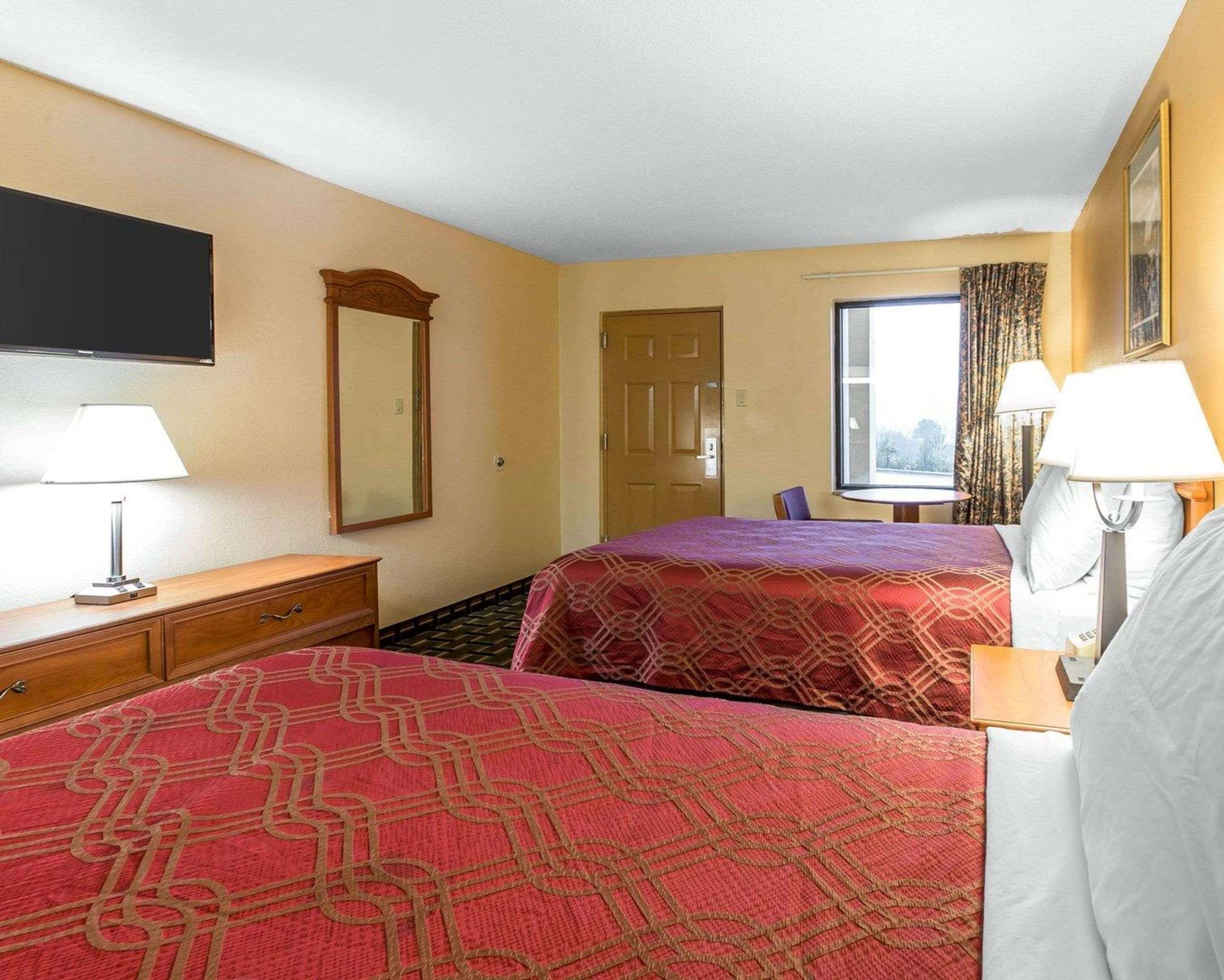 A hotel room with two beds, a TV, a desk, a chair, and a window with curtains.