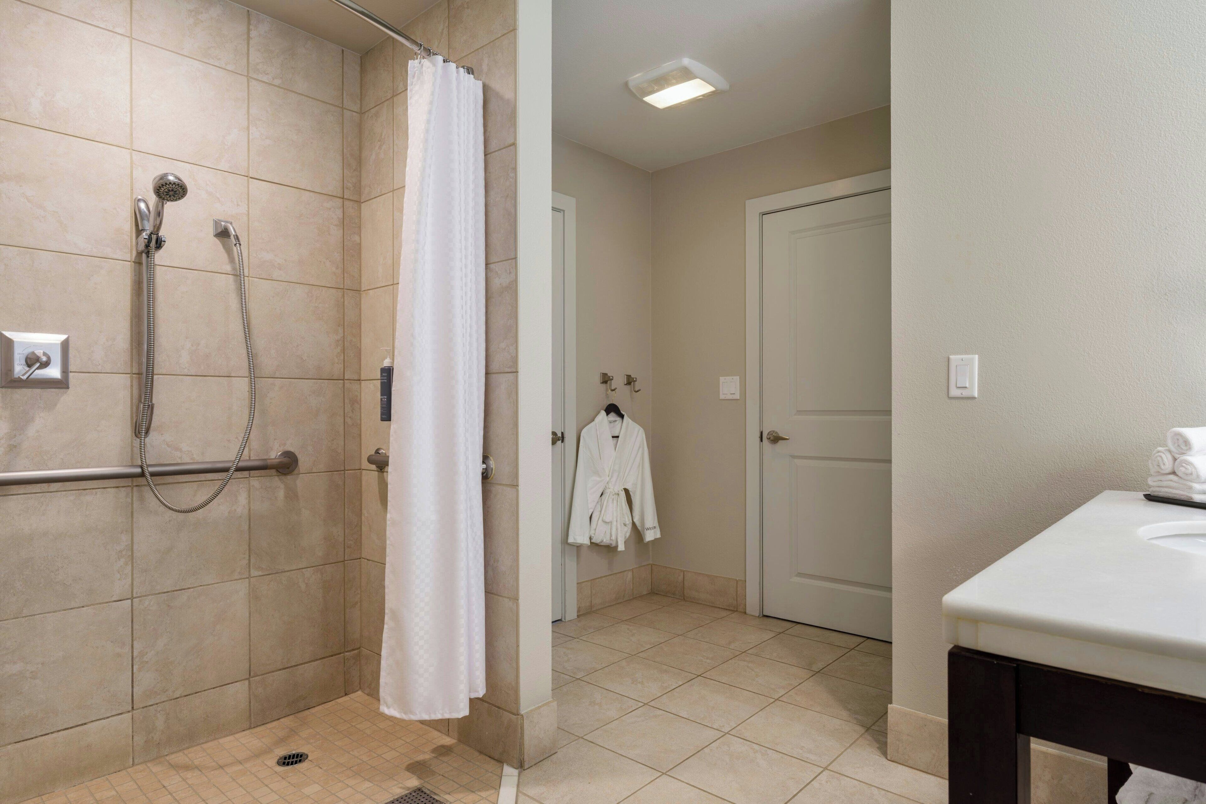 A bathroom with a shower area, a white bathtub, and a sink with a mirror.