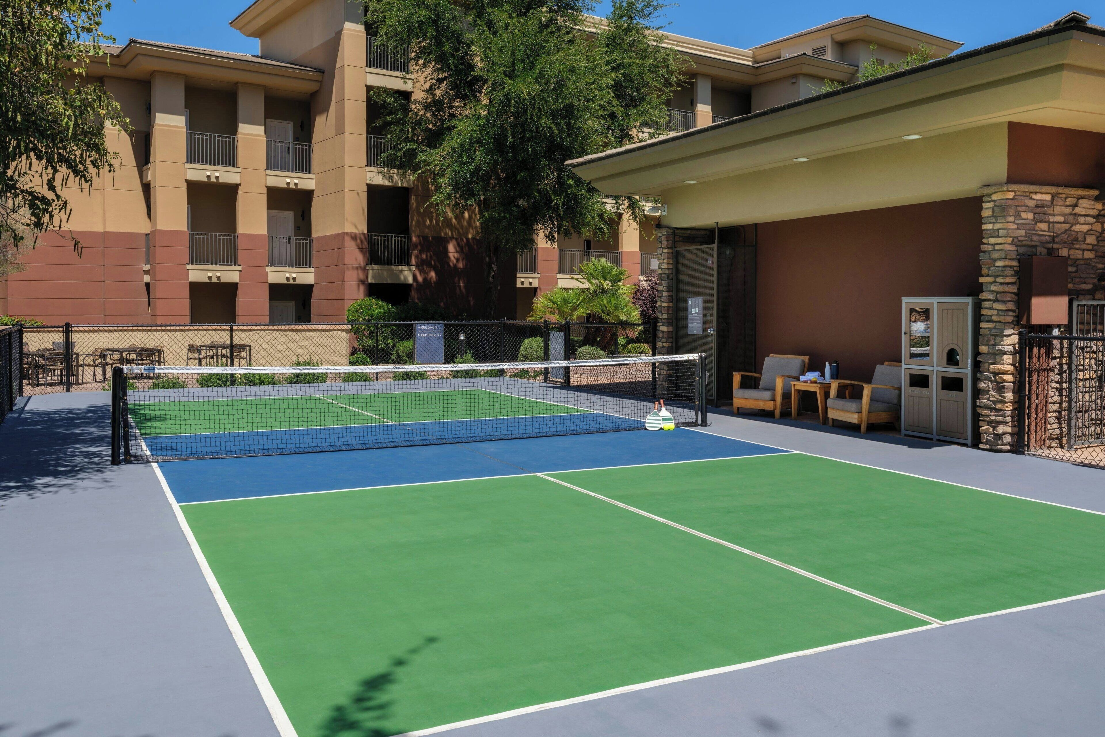 Un court de tennis en plein air, doté d’un filet, entouré d’une clôture et d’arbres.