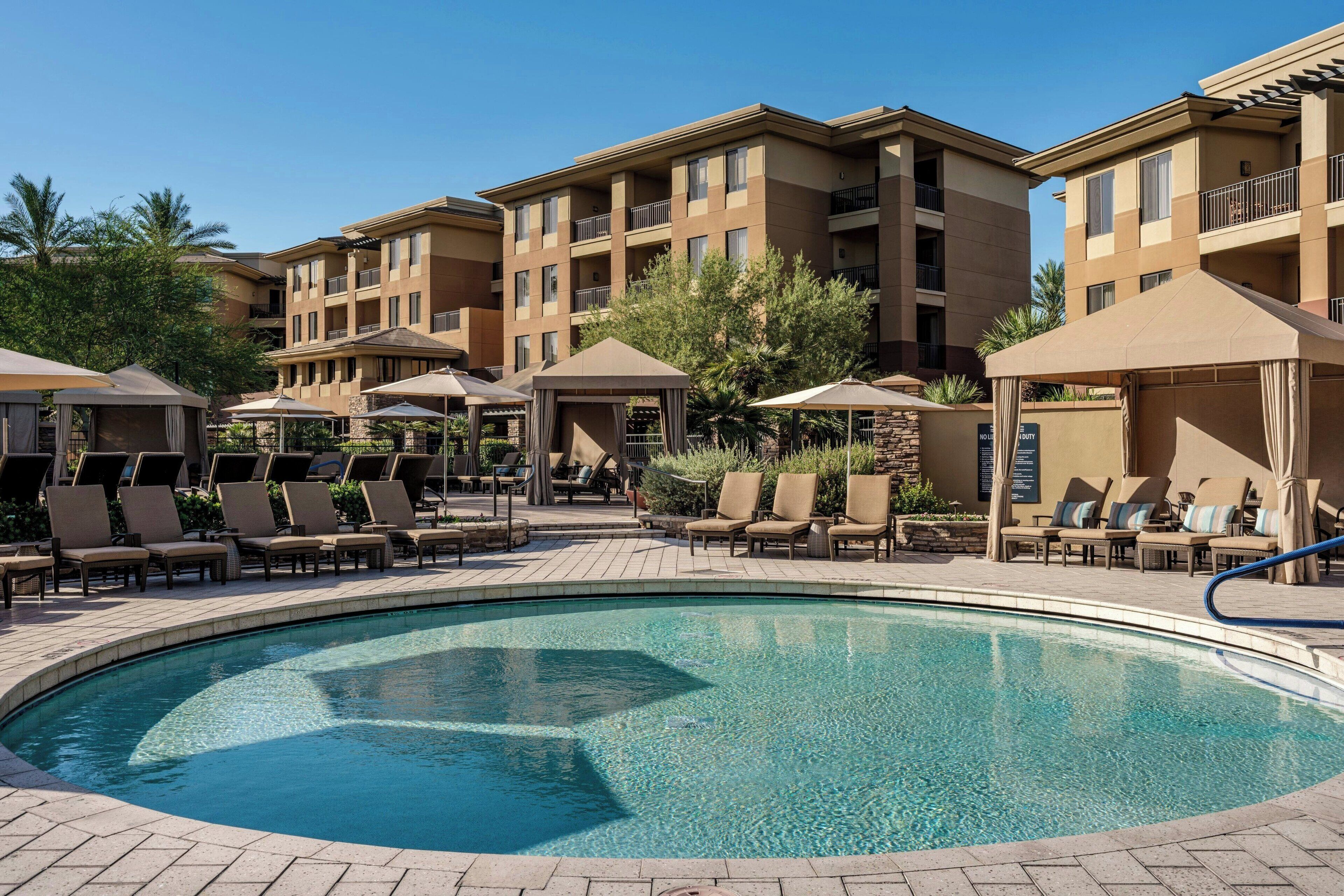 A pool area with lounge chairs and umbrellas, surrounded by multi-story buildings with balconies.