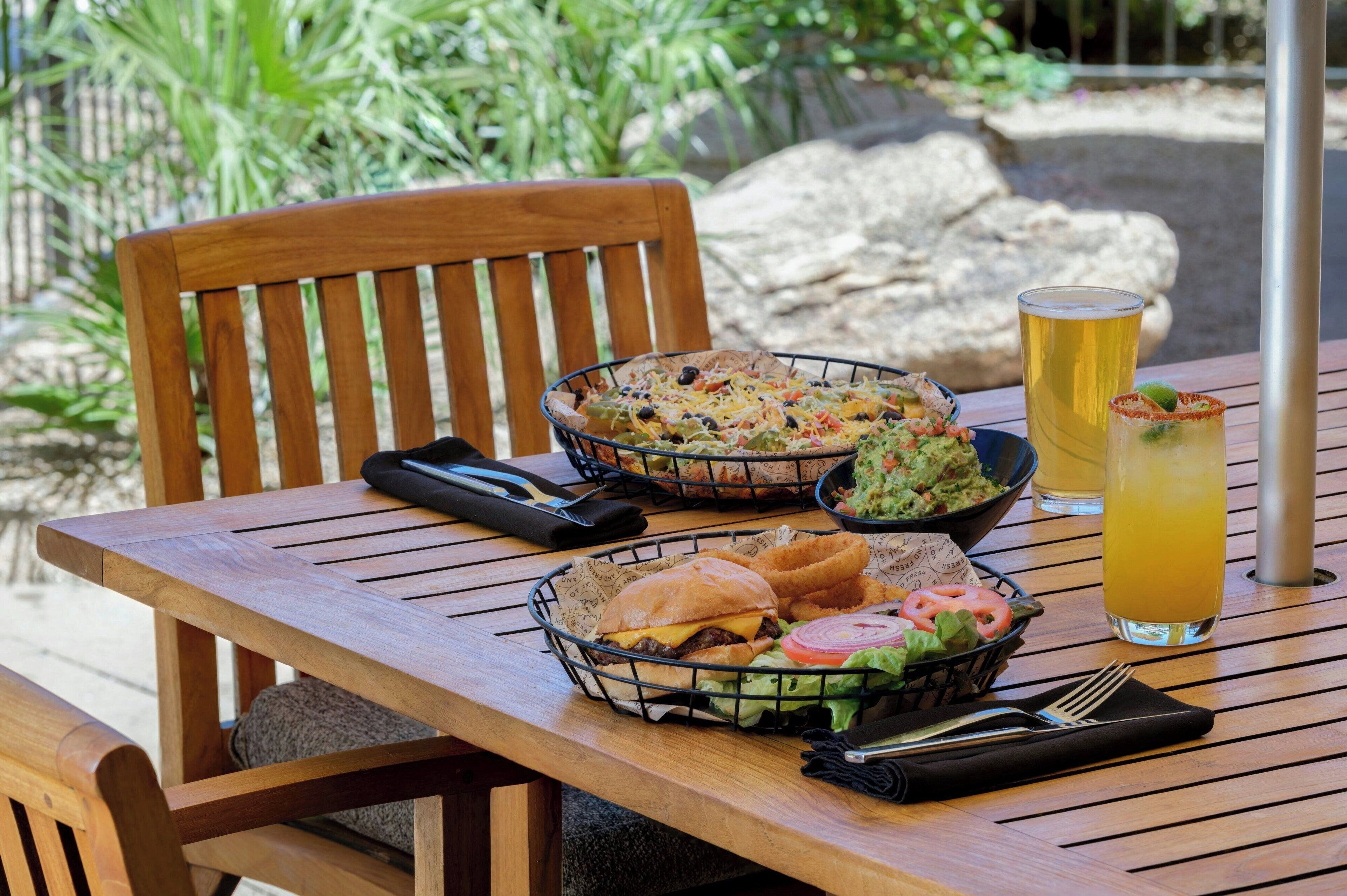 A wooden table with a basket of food, a glass of beer, and a drink with a lime wedge.