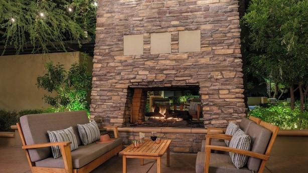 An outdoor seating area with a stone fireplace, cushioned chairs, and a small table. - The Westin Kierland Villas, Scottsdale (Scottsdale)