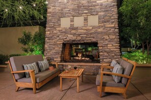 Un espacio al aire libre con chimenea de piedra, sillas acolchadas y una pequeña mesa.