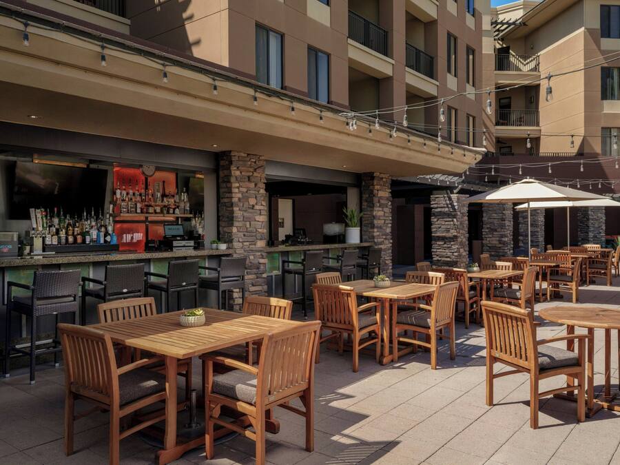 Eine Außenpatio mit Holztischen und -stühlen, einer Bar mit Flaschen sowie einer Stein-Fassade.