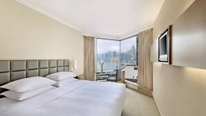 A hotel room with a large bed, a television mounted on the wall, and a view of a cityscape through large windows. - The Kowloon Hotel (Kowloon)