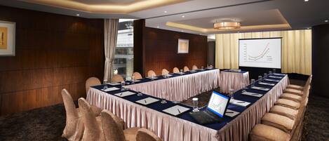 A conference room with a long table, chairs, a laptop, and a presentation screen.