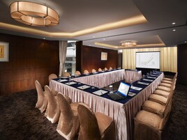 A conference room with a long table, chairs, a laptop, and a presentation screen.