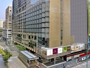 A modern high-rise building with a reflective glass facade, a ground-level coffee shop, and a pedestrian walkway. - The Kowloon Hotel (Kowloon)