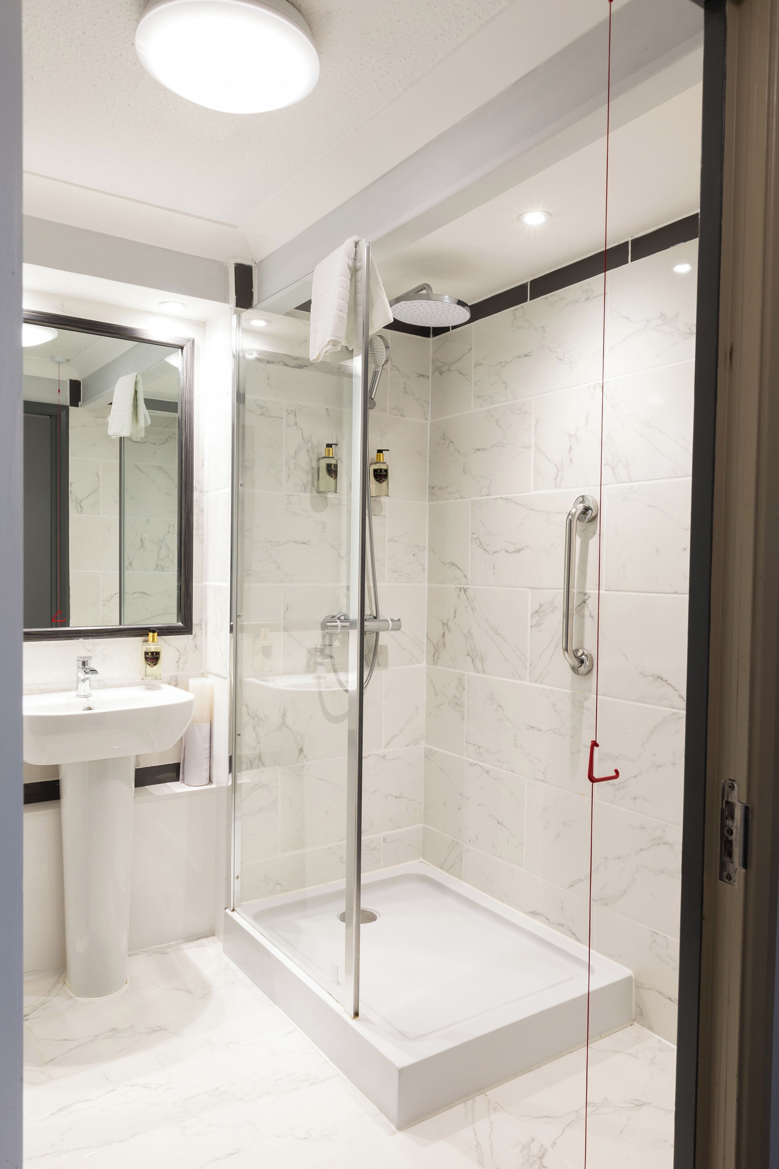 Ein modernes Badezimmer mit einer gläsernen Dusche, weißen Marmorfliesen und einem großen Spiegel.