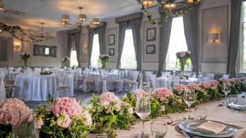 Une salle de banquet avec des tables rondes dressées pour un événement formel, agrémentée de compositions florales et de verres transparents.