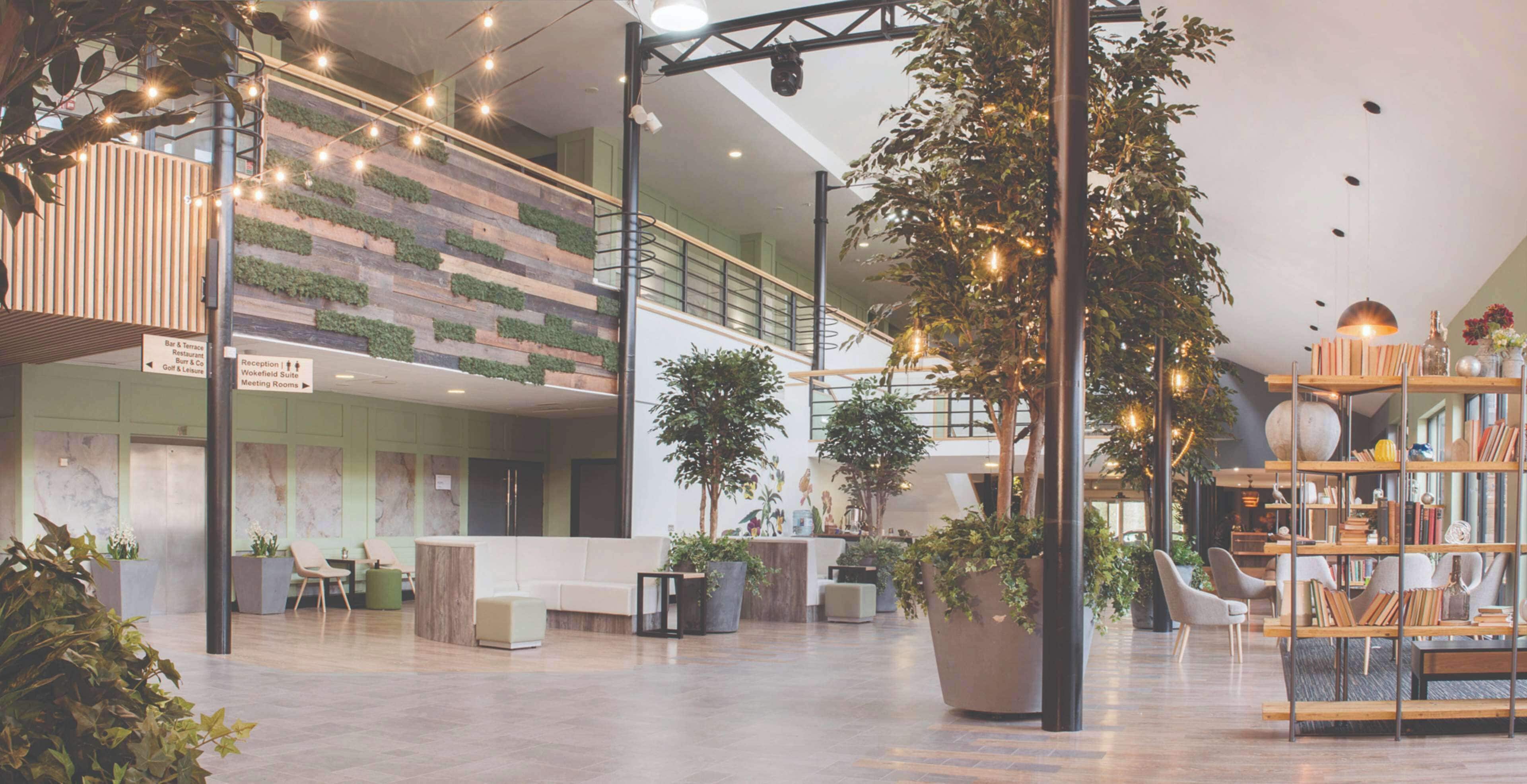 A spacious lobby with a reception desk, seating areas, a staircase, and a bookshelf.