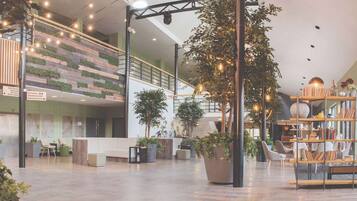 A spacious lobby with a reception desk, seating areas, a staircase, and a bookshelf.