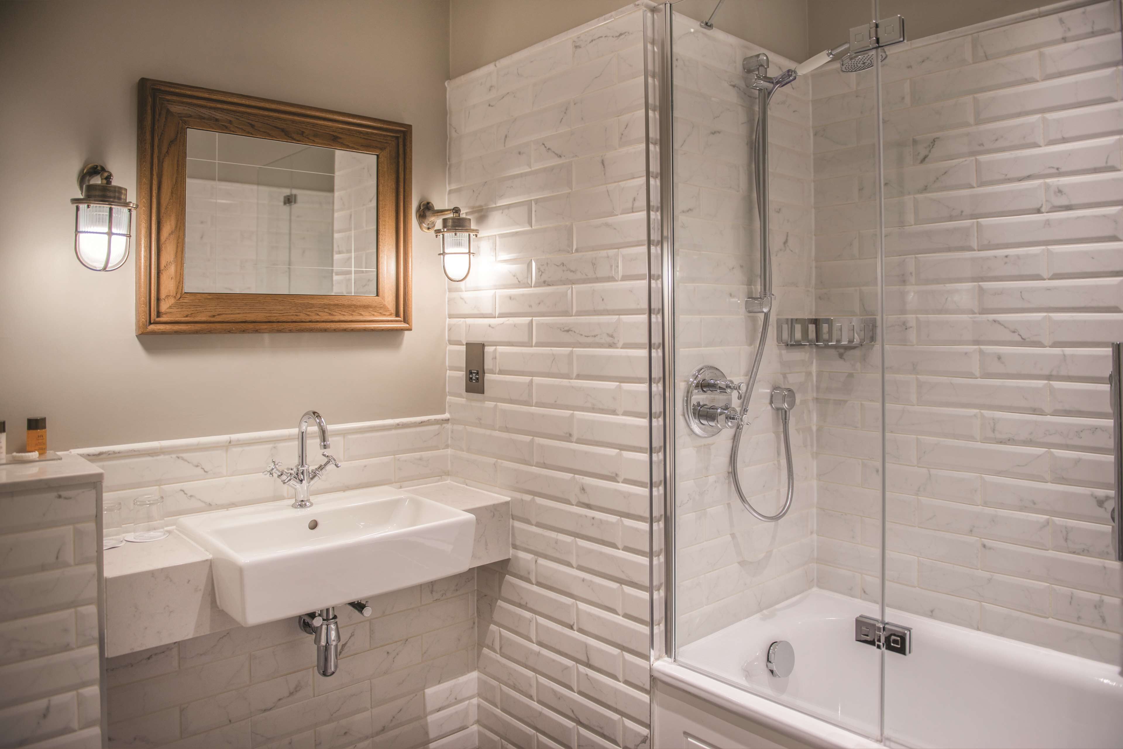 A bathroom with a white marble sink, a wooden-framed mirror, and a glass-enclosed shower.