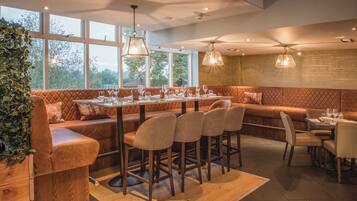 Un restaurante con una larga mesa de madera, asientos acolchados e iluminación colgante.