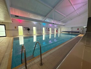 An indoor swimming pool with clear water, a tiled floor, and a ceiling with visible structural beams.