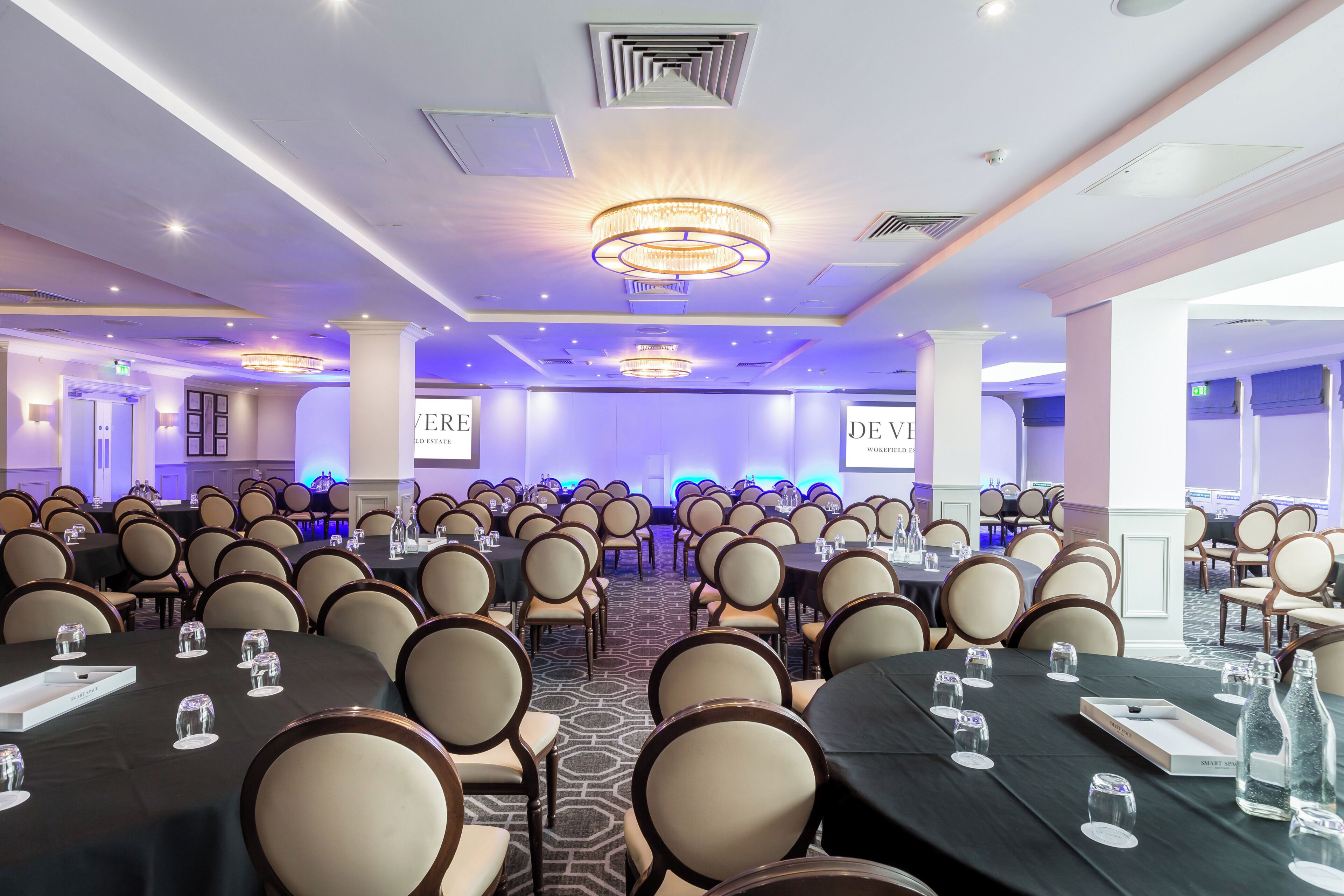 A conference room with multiple tables and chairs, equipped with water bottles and glasses.