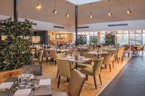A spacious dining area with multiple tables and chairs, large windows, and hanging pendant lights.